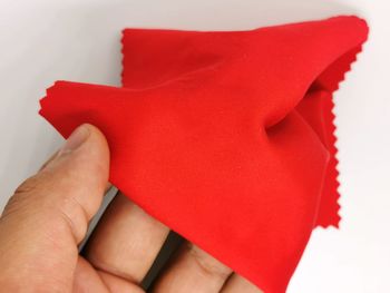 Close-up of hand holding red paper over white background