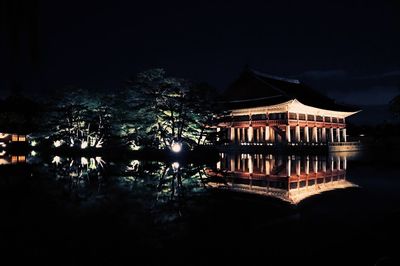 Illuminated building by lake against sky at night