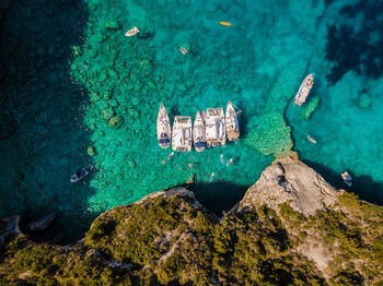 High angle view of rock formation and sailboats in sea with sea caves and bright blue water.