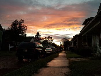 Cars on street amidst buildings against sky during sunset