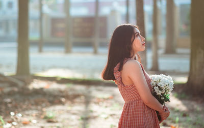 Side view of young woman holding bouquet while standing at park