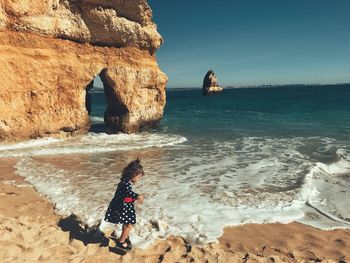 Girl standing on shore at praia do camilo against rock formation