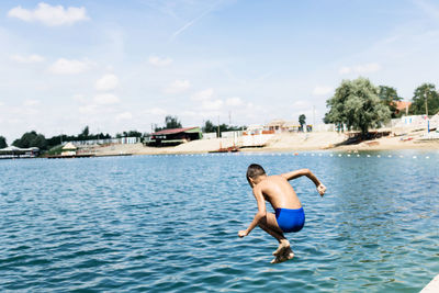 Full length of shirtless boy diving in sea against sky