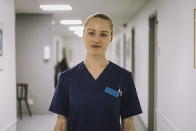 Portrait of smiling female healthcare worker standing in corridor at hospital