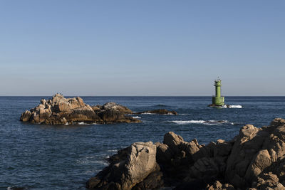 Lighthouse on rock by sea against clear sky