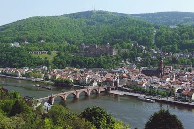 Arch bridge over neckar river by heidelberg castle and old town against tree mountains