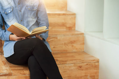 Midsection of woman reading book at home