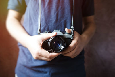 Midsection of man holding digital camera against wall