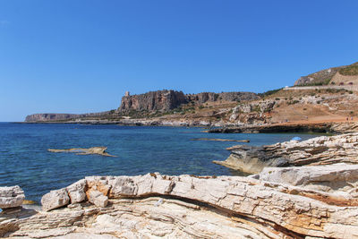 Scenic view of sea and rocks against clear blue sky