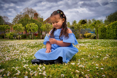 A little girl sitting on the grass during springtime in a field of daisies