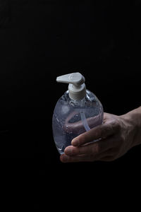 Close-up of hand holding glass bottle against black background