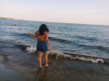 Rear view of woman standing on beach against clear sky