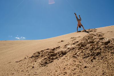 Rear view of shirtless man doing handstand against blue sky during sunny day