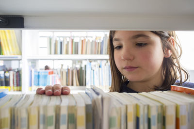 Young girl selecting books from library bookshelf