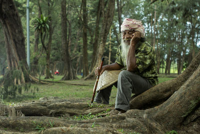 Portrait of senior man with hat while sitting on field against trees in forest