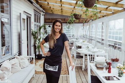 Portrait of smiling female owner standing by chair in restaurant