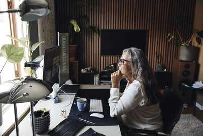 Side view of smiling businesswoman with hand on chin doing video call at home office