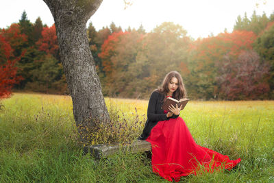 Full length of young woman reading book while sitting on bench at park