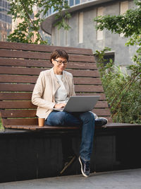 Freelance business woman sits in park with laptop and take away cardboard cup of coffee. 