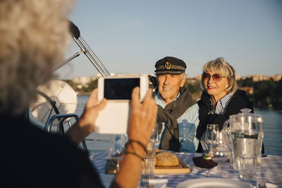 Cropped image of woman photographing senior couple sitting in boat on sunny day