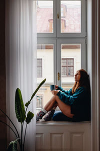 Woman sitting on the big windowsill with a cup of tea