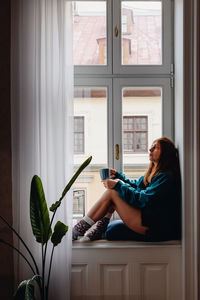 Rear view of young woman using mobile phone while sitting at home