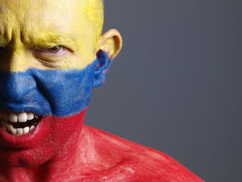 Close-up portrait of angry man with venezuelan flag body paint against gray background