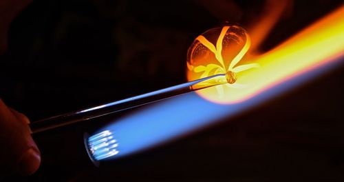 Cropped image of woman making glass with flaming torch in factory