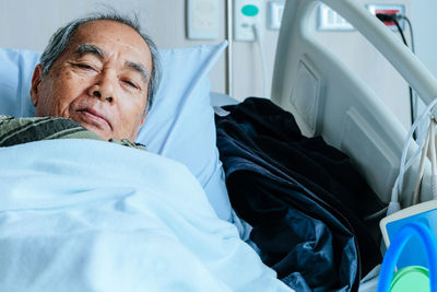 Portrait of senior man lying down on bed at hospital