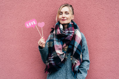 Portrait of smiling woman holding props against wall in winter