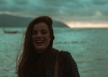 Close-up of smiling young woman standing at beach against sky