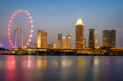 Illuminated singapore flyer and buildings by sea in city at night