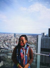 Smiling woman standing on balcony against sky in city