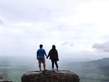 Rear view of men standing on rock looking at mountain against sky