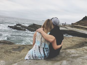 Rear view of couple sitting with arms around on rocky shore