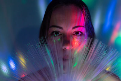 Close-up portrait of young woman holding illuminated fiber optic in darkroom