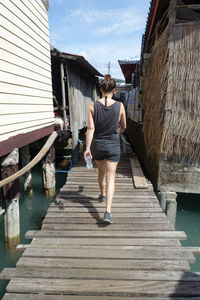 Rear view of woman walking on pier amidst stilt houses