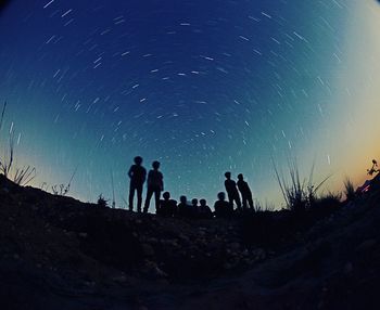 Fish-eye view of silhouette people on field against star trails