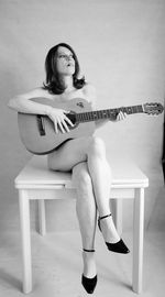 Full length of sensuous woman holding guitar while sitting on table
