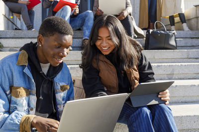 Smiling woman studying with friend through laptop on campus