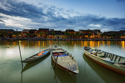 Boats moored at waterfront against cloudy sky
