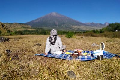 Man sitting on table by field against sky