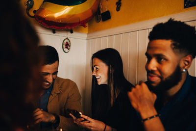 Young woman and man sharing mobile phone while sitting by friend at restaurant