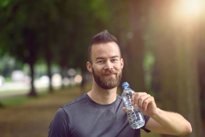 Portrait of handsome athlete drinking water in park