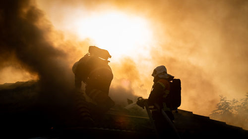 Firefighters spraying water on burning roof against sky