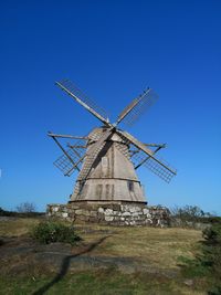 Low angle view of traditional windmill on field against clear blue sky