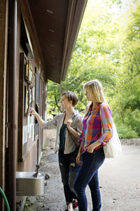 Friends reading signboard in forest while standing against cottage in forest