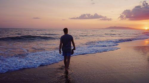 Rear view of man standing at beach during sunset