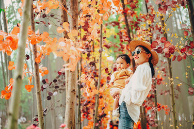 Smiling mother with son standing against autumn tree in forest