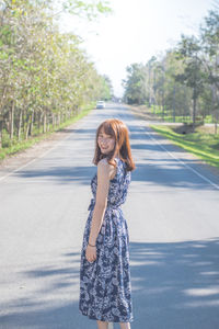 Portrait of woman standing on road against trees